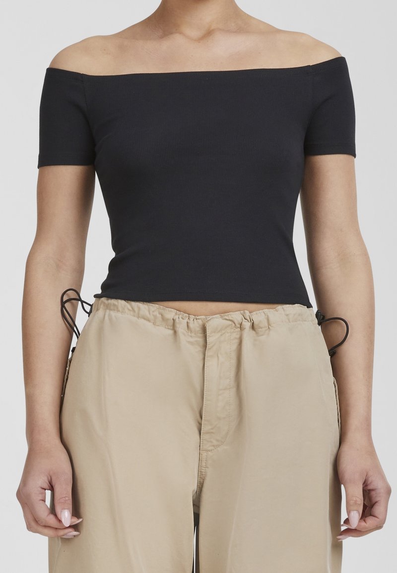 Black ribbed off-the-shoulder top with short sleeves, paired with beige drawstring pants, creating a casual and layered look.