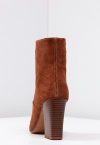 Botte de cheville en daim marron avec un bout rond, un haut talon bloc et un détail de couture verticale à l'arrière. Semelle lisse et talon texturé.