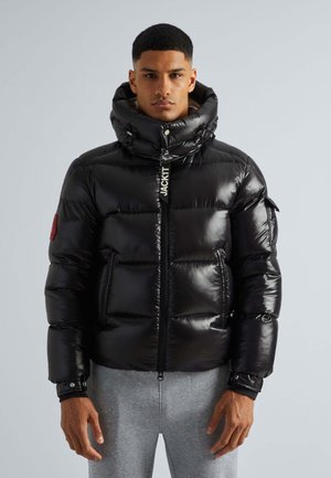 Black puffer jacket with shiny, quilted surface, high collar, front zip, and logo detail. Features side pockets and elastic cuffs.