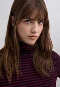 Long-sleeved, fitted turtleneck top featuring dark purple and black stripes. Model with long, straight brown hair and blunt bangs.