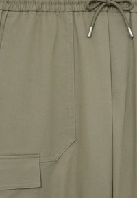 Pantalones de chándal caqui con una tela texturizada, que presentan una cinturilla elástica, cierre con cordón y un detalle de bolsillo lateral.