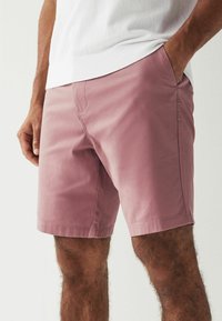 Lyserøde, letvægts shorts med en glat tekstur, sidelommer og en ren søm. Båret med en hvid, ribbet t-shirt med rund hals.