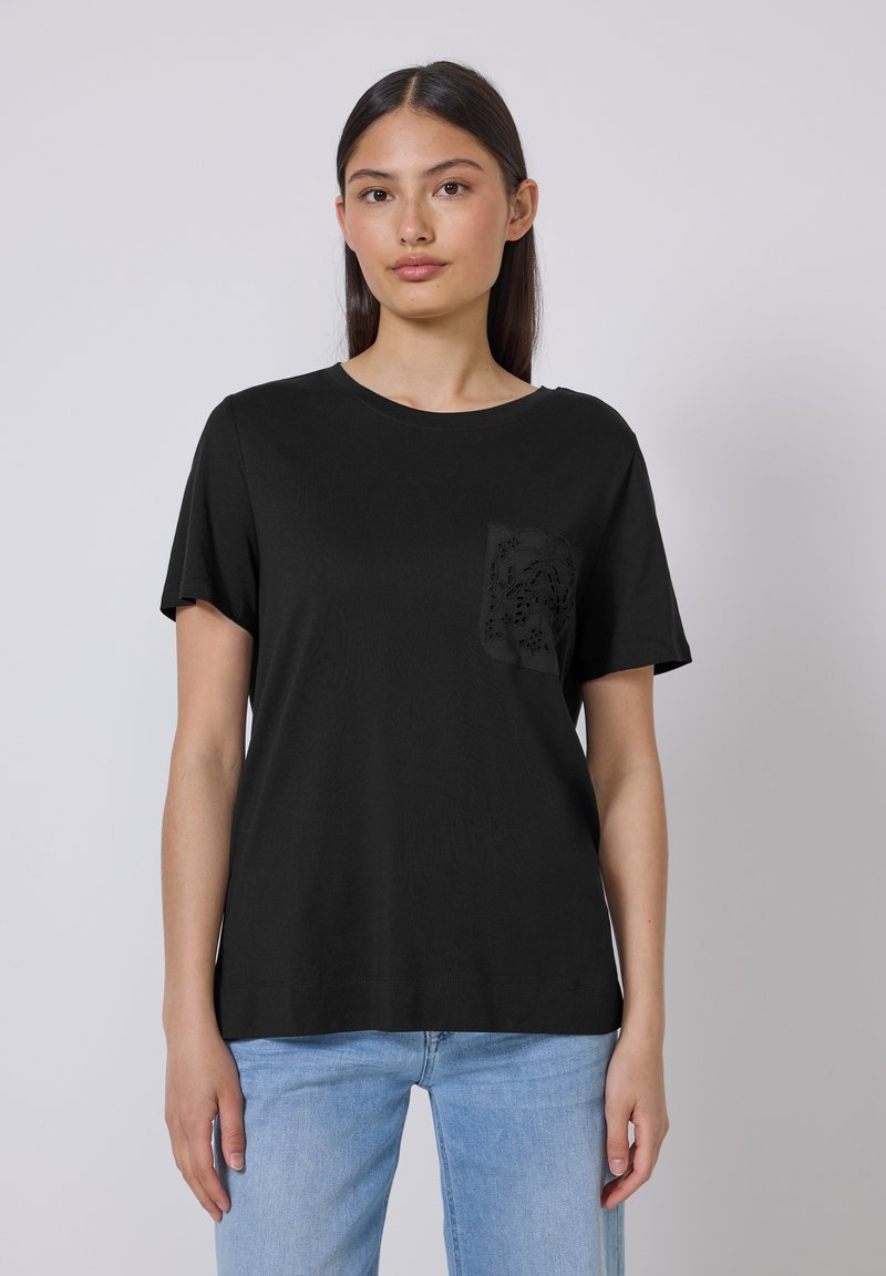 Sort kortærmet t-shirt lavet af bomuld med en lomme med et blondelignende udskæringsdesign. Glat tekstur og standard rund hals.