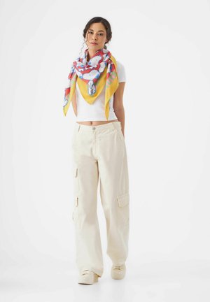 Lässiges Outfit aus Baumwollmischung mit einem weißen Cropped-Top, kremfarbigen Cargo-Shorts mit Taschen und einem bunten, gemusterten quadratischen Schal um den Hals gebunden.