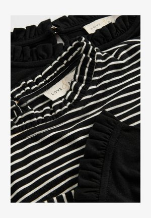 Țesătură cu dungi alb-negru, cu decolteu și margini la mâneci volărite, având o textură moale și modele contrastante. Eticheta brandului este vizibilă.