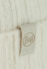 Light beige knit hat featuring a textured pattern and a fabric label with the "Buff" logo. Soft, fuzzy material with a ribbed design.