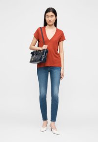 Κόκκινο μπλουζάκι V-λαιμόκοψη, σκούρο μπλε τσάντα χειρός με λεπτομέρεια ζώνης, μπλε στενά τζιν και λευκές μυτερές γόβες. Απλός σχεδιασμός και casual στυλ.