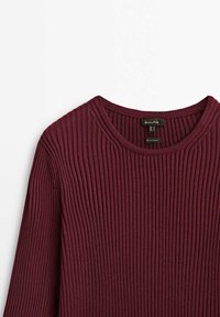 Bordowy sweter prążkowany z okrągłym dekoltem i długimi rękawami. Teksturowany materiał z pionowymi żeberkami i widoczną metką wewnątrz.