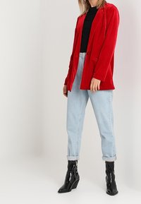 Blazer en velours rouge à la coupe ajustée, associé à un jean taille haute bleu clair et des bottines en cuir verni noir.
