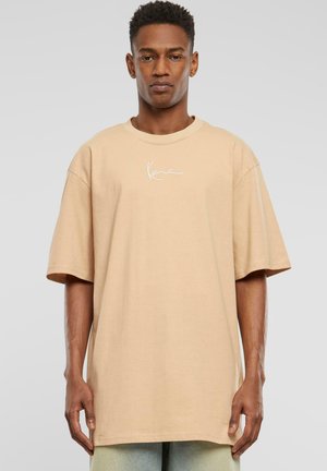 Beige oversized cotton t-shirt with short sleeves. Features a white signature logo on the chest. Smooth texture and relaxed fit.