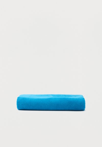 Λαμπερή μπλε διπλωμένη πετσέτα απλωμένη επίπεδα σε λευκό φόντο, που δείχνει απαλή υφή και καθαρές άκρες.