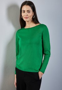 Pull vert à manches longues en tricot doux, avec un col bateau et un ourlet côtelé. Associé à un pantalon noir, style minimaliste.