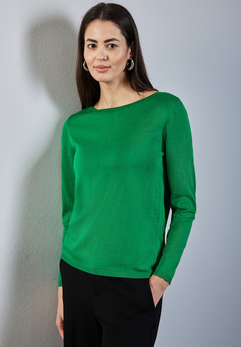 Pull vert à manches longues en tricot doux, avec un col bateau et un ourlet côtelé. Associé à un pantalon noir, style minimaliste.