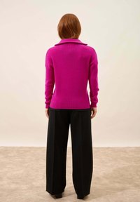 Dopasowany, głęboki różowy sweter z kołnierzykiem; prążkowana struktura i długie rękawy. Połączony z szerokimi, czarnymi spodniami, tworzy smukłą sylwetkę.