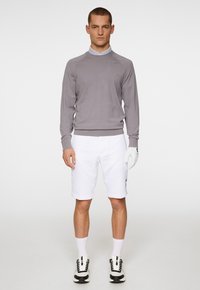 Grå stickad tröja, vita shorts och svartvita sneakers. Handske på vänster hand. Enkel design med ribbade muddar och krage.