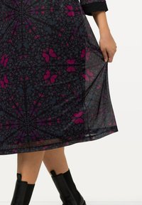 Durchsichtiges schwarzes Kleid mit einem mehrfarbigen Schmetterlingsmuster in Rosa- und Blautönen, das eine ausgestellt Silhouette und schwarze Manschetten aufweist.