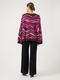 Pull oversize à motif ondulé rose et marron, fabriqué en matière douce et duveteuse. Associé à un pantalon large noir et des talons.