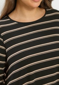 Top a rayas en negro y beige con textura acanalada, cuello redondo y rayas diagonales que crean un patrón audaz.