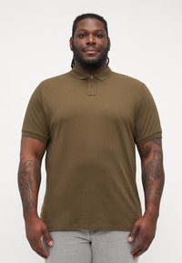 Oliven grønn polo skjorte med korte ermer, krage og tre knapper. Laget av glatt stoff, slimfit design, minimal detaljer.