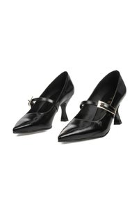 Zapatos de charol negros con punta afilada, una tira delgada con herrajes dorados y un tacón ligeramente curvado. Textura suave en todo el zapato.