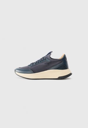 Sneakers with a navy mesh upper, dark blue accents, and a light beige textured sole. Features curved design and prominent lacing.