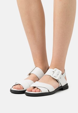 White leather sandals with a wide front strap, an adjustable ankle strap featuring a buckle, and a black sole. Unisex design.