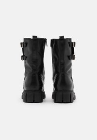 Bottes en cuir noir avec un design mi-mollet, deux boucles latérales et une semelle en caoutchouc texturée à profil angulaire.