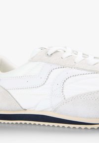 Zapatilla blanca con parte superior de ante y textil, con costuras tonales, cordones planos blancos y una suela delgada azul marino con un acabado texturizado.