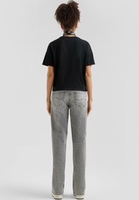 Zwarte cropped t-shirt met korte mouwen, gecombineerd met high-waisted, lichtgrijze denim jeans met achterzakken en een rechte pijp.