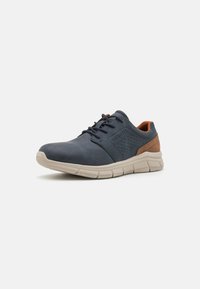 Chaussures synthétiques bleu marine avec une texture lisse, présentant un panneau latéral perforé, des accents marron et une semelle en caoutchouc beige.