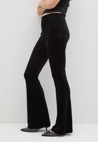 Pantaloni neri a campana realizzati in un morbido e elasticizzato tessuto, con una superficie liscia e una vita alta, abbinati a tacchi a spillo neri con borchie.