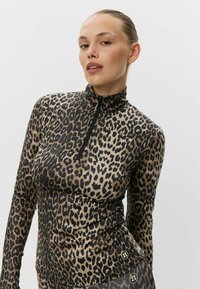 Camiseta de manga larga con estampado de leopardo, cuello alto y media cremallera. Confeccionada con un material suave y elástico, en una combinación de colores negro y marrón.