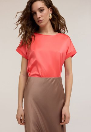 Koraal satijnen top met opgerolde mouwen gecombineerd met een bruine satijnen rok. Gladde textuur; ontspannen pasvorm; geen patronen of opmerkelijke hardware details.