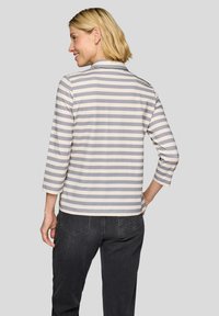 Striped long-sleeve top in light gray and white, featuring a shirt collar and mid-length sleeves, paired with dark jeans.