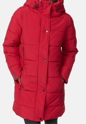 Femme portant un long manteau d'hiver matelassé rouge avec une capuche, des boutons-pression sur le devant et des poches latérales zippées, les mains à l'intérieur.