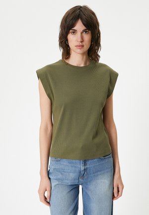 Top corto a maniche corte verde oliva con texture a coste, scollatura a girocollo e spalle imbottite, abbinato a jeans azzurri chiari.