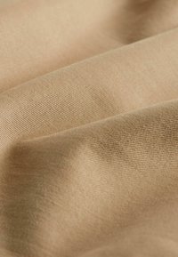 Beiger Stoff mit glatter Textur, der subtile diagonale Webmuster und eine weiche, natürliche Drapierung zeigt.