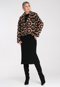 Brązowa i czarna, wzorzysta kurtka do pasa z okręgami, połączona z czarną, prążkowaną midi spódnicą i czarnymi, do kolan wysokimi botkami.