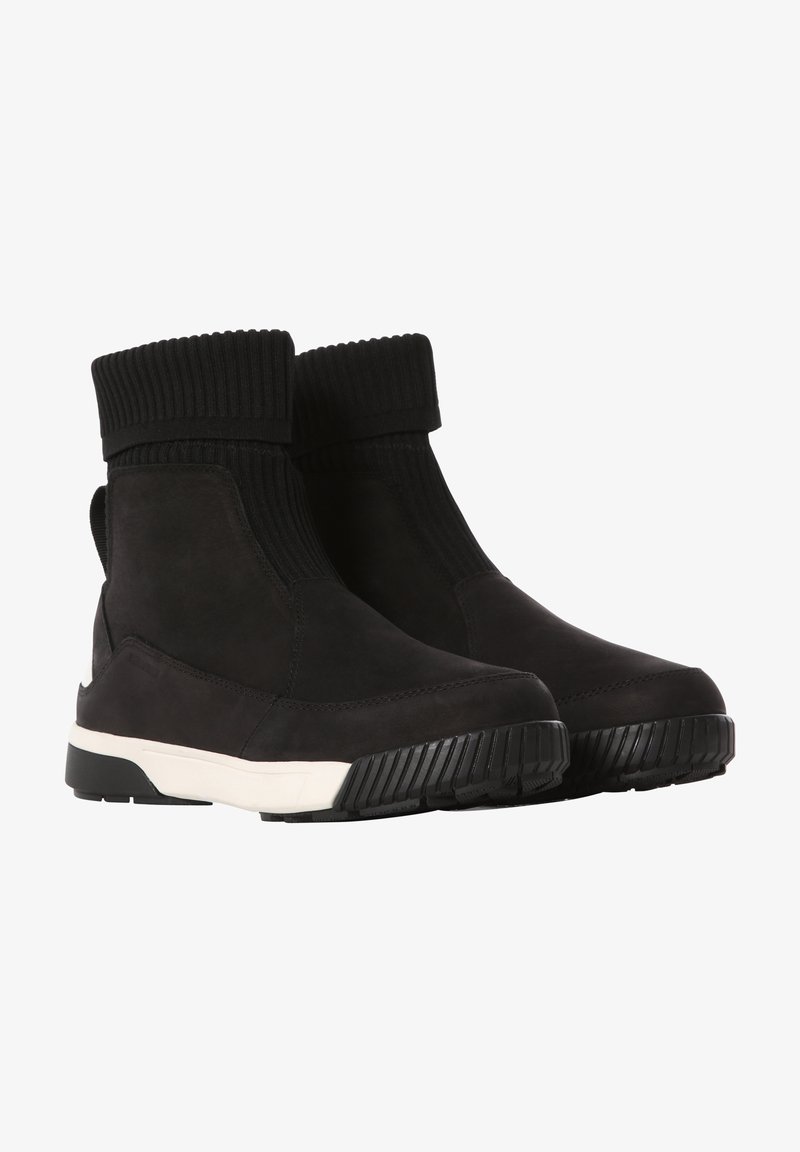 Black ankle boots with a ribbed knit upper and smooth suede lower, featuring a white sole and textured rubber outsole for grip.