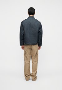 Σκο ύρα τζιν μπουφάν με κλασική γραμμή, κουμπιά ως διακοσμητικά και εμφανή ραφές. Συνδυασμένο με φαρδιά ανοιχτόχρωμα χακί παντελόνια cargo.