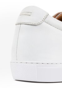 Biały skórzany obcas sneakersa o gładkiej teksturze, kontrastowe szwy oraz gumowa podeszwa z teksturowanym wzorem antypoślizgowym.
