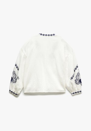 Valkoinen teksturoitu paita pitkillä puffi hihnoilla. Varustettu tummansinisin brodeeratuin yksityiskohdin hihansuissa ja kaula-aukossa. Neliömäinen leikkaus.