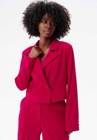Korte, dubbelgerijgde blazer in helder fuchsia met lange mouwen, ingeknipte revers en knopen aan de voorkant. Gladde stoftextuur.