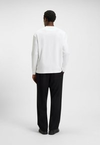 White long-sleeve shirt with a relaxed fit, paired with black wide-leg trousers. The fabric appears smooth with a slight sheen.