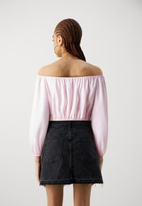Off-shoulder rosa bluse med luftige ærmer, innsnevret midje, kombinert med en slitt svart denim miniskjørt med baklommer.