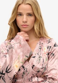 Vestido de satén rosa con patrones florales, diseño de escote en v y detalles plisados. Textura suave con mangas largas que presentan acentos florales.