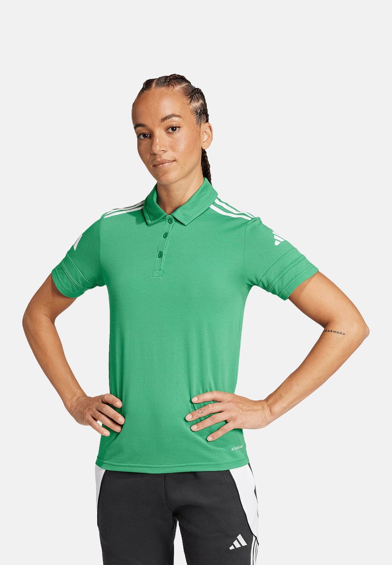 Polo verde con colletto, caratterizzato da strisce bianche sulle spalle. Tessuto liscio, vestibilità standard, abbinato a pantaloni neri.