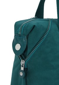 Teal fabric bag with textured surface, featuring a prominent zipper and circular leather tag. Includes main handle and contrasting zipper detail.