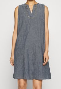 Robe sans manches en lin gris avec un col en V et une coupe décontractée à texture subtile, arrivant à mi-cuisse. Design minimaliste sans motifs.