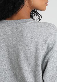 Felpa grigio melange con tessuto morbido e strutturato. Presenta un classico scollo a girocollo e una vestibilità comoda, con dettagli a coste al collo.